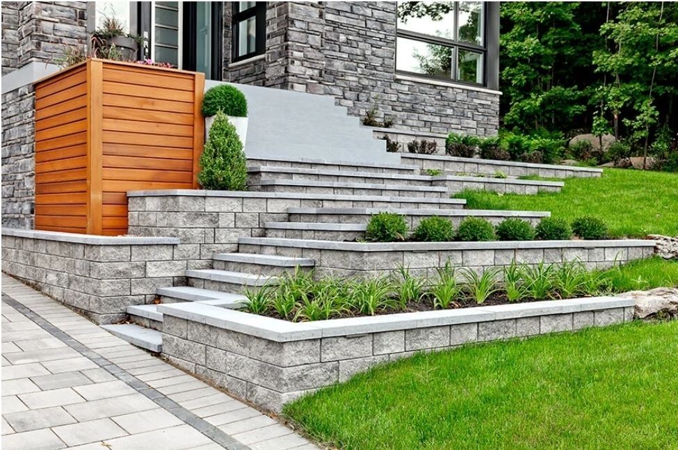 Modern house exterior with landscaped stone steps, greenery, wooden paneling, and lush grass lawn.